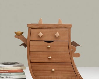 May include: A wooden dresser with four drawers, featuring a whimsical design. The dresser has a light brown finish, star-shaped drawer pulls, and decorative horns and wings. A small gold-colored bowl is held on the side.