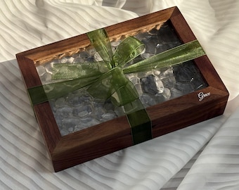 May include: A rectangular wooden box with a clear top, filled with gray stones, and tied with a green ribbon. The box has a dark brown frame and the word "Grace" is printed on the side.