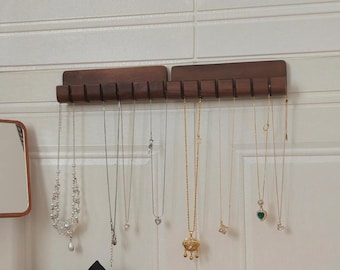 May include: Wooden necklace organizers with multiple necklaces hanging from them. The necklaces are silver and gold, with various pendants. A pearl necklace and bracelet are on a wooden surface. A black and white scrunchie and a black scrunchie are also on the surface.