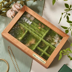 May include: A wooden jewelry box with a glass top and green velvet lining. The box has multiple compartments for storing rings, earrings, and other small jewelry items. The box has a gold label that reads "Hakuna Matata".
