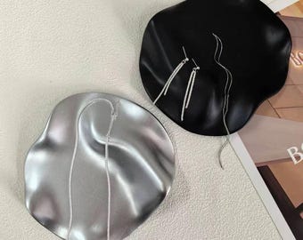 May include: Two irregularly shaped jewelry trays, one silver and one black, display silver earrings and a necklace. The trays sit on a light-colored surface, showcasing the jewelry's delicate design and contrasting colors.