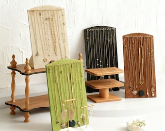 May include: A collection of wooden jewelry display stands in various styles and colors. The stands hold necklaces and earrings. The displays are made of wood, with some featuring a green fabric backing. The jewelry is gold-toned.