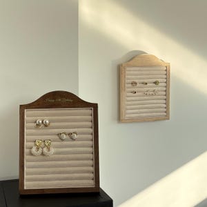 May include: Two wooden earring display boards with beige velvet inserts. One board is dark brown with the text "Happy 30th Birthday" and holds pearl and gold earrings. The other is light wood and displays various gold earrings.