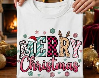 Può includere: T-shirt bianca con la scritta "MERRY Christmas" in un design festoso e colorato. La parola "MERRY" include un cappello di Babbo Natale, strisce e un motivo a scacchi. "Christmas" è in gradiente rosa con fiocchi di neve e stelle.