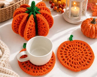 Può includere: Una zucca arancione all'uncinetto con un gambo verde, due sottobicchieri rotondi all'uncinetto a forma di zucca arancione e una tazza in ceramica bianca. Un sottobicchiere è sotto la tazza, l'altro è piatto accanto con un motivo a punto aperto.