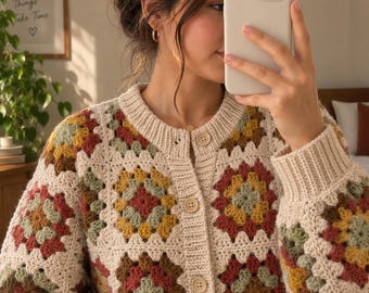 Può includere: Un cardigan all'uncinetto a maniche lunghe con motivo a piastrelle granny in tonalità tenui di crema, giallo senape, verde salvia e terracotta. Il capo presenta un girocollo a coste, polsini a coste e chiusura frontale con bottoni beige.