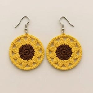 Peut inclure: Une paire de boucles d'oreilles faites à la main en crochet, représentant des tournesols. Les boucles d'oreilles ont un anneau extérieur jaune et un centre marron, avec des crochets d'oreilles argentés. Les pétales de tournesol sont détaillés.