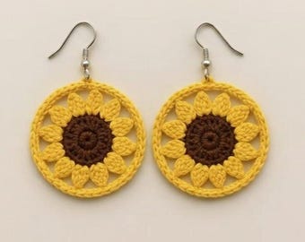 Può includere: Un paio di orecchini all'uncinetto fatti a mano con un design a girasole. Gli orecchini hanno un anello esterno giallo e centri marroni, con ganci per le orecchie color argento. I petali di girasole sono dettagliati.