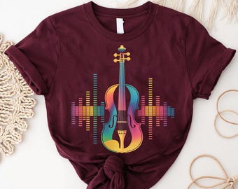 May include: A maroon t-shirt with a vibrant violin graphic. The violin is rendered in a rainbow gradient, flanked by sound wave-style bars. The shirt is made of a soft material.