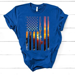 A blue t-shirt with a graphic design depicting an American flag and a sunset landscape.