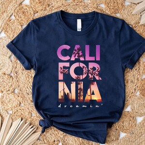 A navy blue t-shirt with the text "CALIFORNIA dreamin'" printed on it, along with a graphic of palm trees and a sunset.