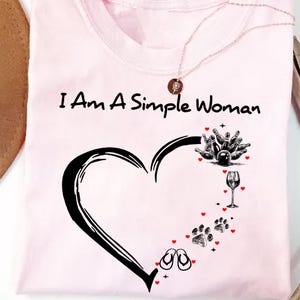 May include: Pink t-shirt with the text "I Am A Simple Woman" and a black heart design. The heart is filled with images of bowling pins, a wine glass, flip flops, and paw prints.