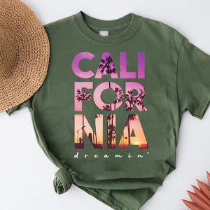 A green t-shirt with the text "CALI FOR NIA" printed on it, along with a straw hat and some decorative items.
