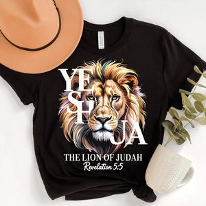 A black t-shirt with a lion's face design and text, along with a beige hat, a white mug, and some greenery.