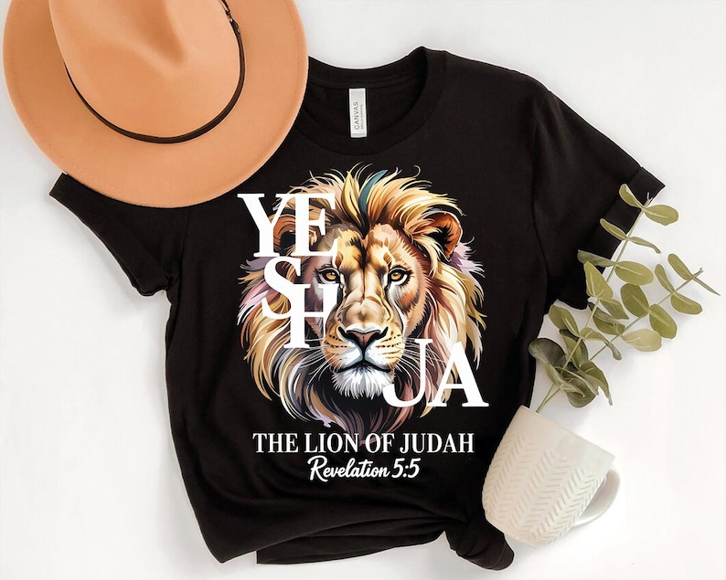A black t-shirt with a lion's face design and text, along with a beige hat, a white mug, and some greenery.
