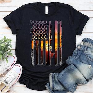 a black t-shirt with a graphic design depicting an American flag and a sunset, along with a pair of jeans and white sneakers.