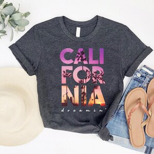 a gray t-shirt with the text "CALIFORNIA dreamin'" printed on it, along with a pair of jeans and a hat.
