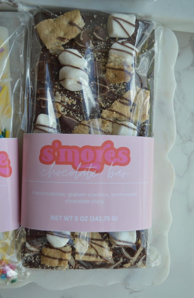 Peut inclure: Une barre de chocolat avec des guimauves, des biscuits Graham et des p&eacute;pites de chocolat mi-sucr&eacute;. La barre est envelopp&eacute;e dans du plastique transparent et porte une &eacute;tiquette rose avec l'inscription "s'mores chocolate bar". Poids net : 141,75 g.