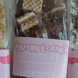 Peut inclure: Une barre de chocolat au croquant de noisettes, avec des barres Kinder Bueno, des gaufrettes et des biscuits Nutella. L'emballage transparent porte une &eacute;tiquette rose avec "Hazelnut Crunch Chocolate Bar". Poids net 141,75 g.