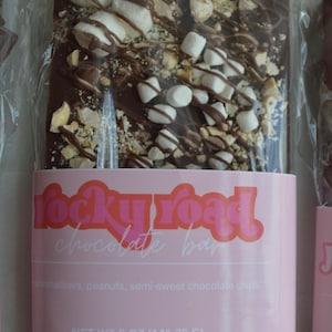 Peut inclure: Barre de chocolat noir Rocky Road avec guimauves, cacahu&egrave;tes et p&eacute;pites de chocolat mi-sucr&eacute;. Emball&eacute; dans du plastique transparent avec une &eacute;tiquette rose &laquo; rocky road chocolate bar &raquo;. Poids net 141,75 g.