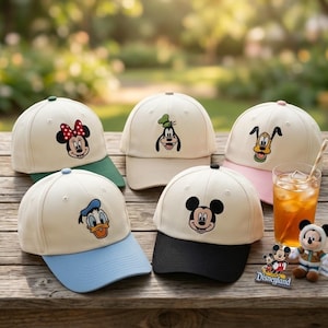 May include: Five baseball caps featuring Disney characters like Mickey Mouse, Minnie Mouse, Goofy, Donald Duck, and Pluto. The caps have cream-colored crowns and colored brims. A glass of iced tea and a Disneyland souvenir are also in the image.