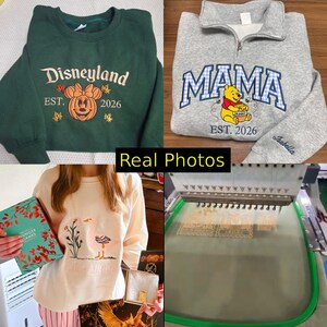 May include: A collection of embroidered apparel including a dark green sweatshirt with a pumpkin design, a grey quarter-zip pullover with a Winnie the Pooh graphic, a cream sweatshirt with a goose illustration, and an embroidery machine in operation.