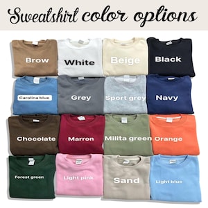 Pu&ograve; includere: Una griglia di felpe girocollo in vari colori, tra cui marrone, bianco, beige, nero, blu Carolina, grigio, grigio sportivo, blu navy, cioccolato, marrone, verde militare, arancione, verde foresta, rosa chiaro, sabbia e azzurro. Il testo in alto recita "Sweatshirt color options."