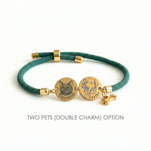 May include: A dark green cord bracelet featuring two gold-toned circular charms engraved with pet portraits and the names Valentino and Chester, accompanied by a small gold-toned bone charm. The text TWO PETS (DOUBLE CHARM) OPTION is visible.