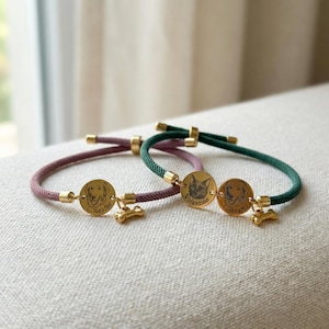 May include: Two adjustable cord bracelets in mauve and dark green, each featuring gold-toned circular metal charms. One charm displays an engraved dog portrait with the name Chester, while the other shows a cat portrait labeled Valentino.