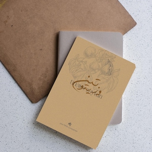 Peut inclure: Un ensemble de carnets et un presse-papiers sur une surface blanche mouchetée. Le carnet supérieur est de couleur beige avec une illustration et du texte. Le presse-papiers est marron avec une pince noire. Le carnet inférieur est gris.