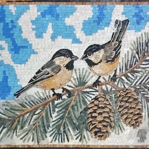 May include: A rectangular mosaic wall art piece featuring two small birds with black heads and tan chests perched on a pine branch. The branch includes green pine needles and two brown pinecones. The background consists of light blue and white tiles.