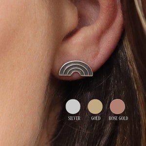 Puede incluir: Un par de pendientes de botón en forma de arcoíris en plata, oro y oro rosa. Los pendientes se muestran en el lóbulo de la oreja de una persona.