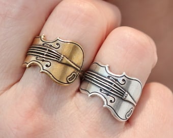 May include: Two silver rings shaped like violins, one with a gold finish, worn on a person's hand.