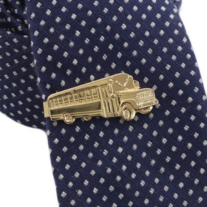 May include: A gold-colored school bus tie clip is displayed on a navy blue tie with a white polka dot pattern. The tie clip is a detailed miniature of a classic school bus.