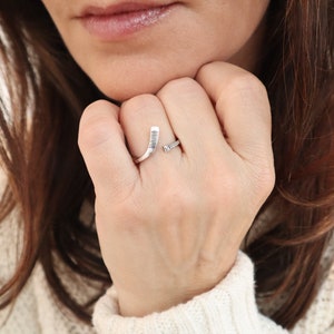 May include: A silver ring shaped like a hockey stick. The ring is worn on a person's finger.
