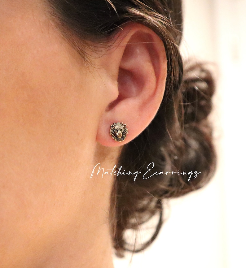 May include: A pair of gold lion head stud earrings. The earrings are small and delicate, and they feature a detailed lion head design. The earrings are shown in a close-up photo, with the lion head facing the viewer. The text "Matching Earrings" is visible in the image.