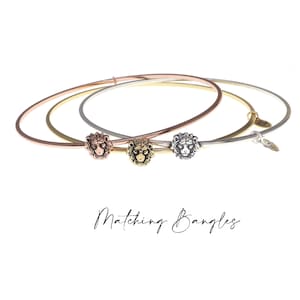 May include: Three matching gold, rose gold, and silver bangles with a lion head charm on each. The bangles are stacked on top of each other. The text "Matching Bangles" is written below the bangles.