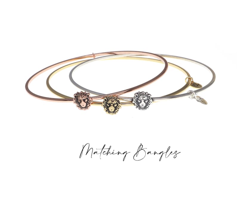 May include: Three matching gold, rose gold, and silver bangles with a lion head charm on each. The bangles are stacked on top of each other. The text "Matching Bangles" is written below the bangles.