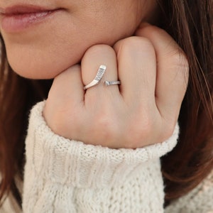 May include: A silver ring with a hockey stick design. The ring is worn on a person's finger.