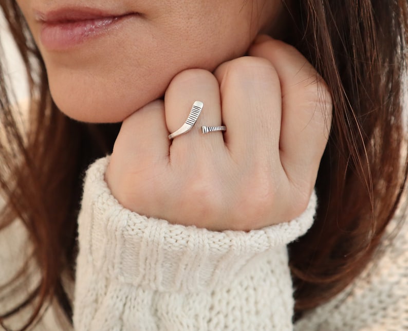 May include: A silver ring with a hockey stick design. The ring is worn on a person's finger.