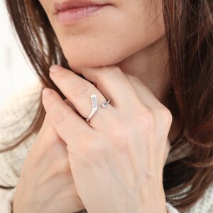 May include: A silver ring with a hockey stick design. The ring is worn on a person's finger.