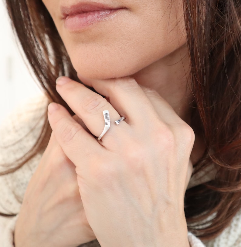 May include: A silver ring with a hockey stick design. The ring is worn on a person's finger.