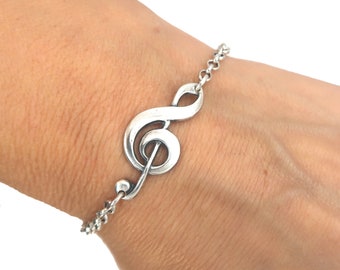 Peut inclure: Un bracelet en argent avec un pendentif en forme de clé de sol. Le bracelet est porté au poignet.
