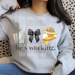 May include: Gray sweatshirt with a graphic design featuring a bee skep, a black bow, and a beekeeper in a yellow suit. The text "he's working" is printed below the graphics.