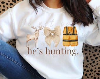 May include: White sweatshirt with a brown deer, a beige bow, and a yellow hunting vest. The text "he's hunting." is printed below the images.
