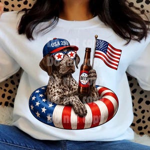 May include: A white sweatshirt featuring a graphic of a spotted dog wearing a blue cap with the text USA 250 and star-patterned sunglasses. The dog holds a beer bottle while sitting in a red, white, and blue striped inner tube with a flag.
