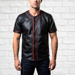 May include: Black leather baseball jersey with red trim on the collar, sleeves, and button placket. The short-sleeved shirt has a button-up front and is paired with dark blue jeans.