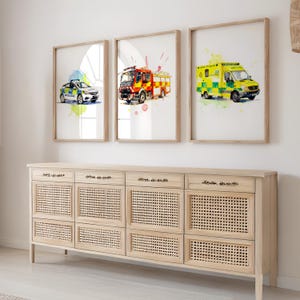 Può includere: Tre stampe ad acquerello incorniciate di veicoli di emergenza: un'auto della polizia, un'autopompa e un'ambulanza. Le stampe sono in cornici di legno e sono esposte sopra un mobile in legno chiaro con pannelli intrecciati.