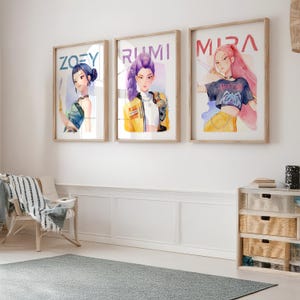 May include: Three framed watercolor prints with the names "ZOEY", "RUMI", and "MIRA" above the portraits. Each portrait features a stylized female figure with unique hairstyles and outfits. The frames are light brown, and the artwork hangs on a white wall.