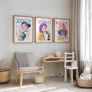 May include: Three framed art prints featuring watercolor illustrations of stylized female figures. Each print has a different name: Zoey, Rumi, and Mira, written in blue. The artwork is displayed in a light-filled room with a chair, desk, and a toy bunny.